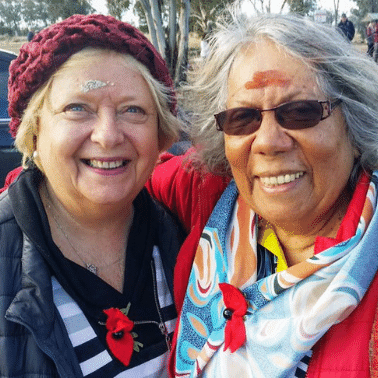 Elderly white Cnadian woman on the right smiles and is embraced by elderly Indigenous woman on left