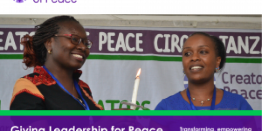 Two African women standing together and smiling with 'peace' banner in background