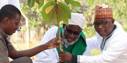 An African Imam and African pastor plant a sapling tree with the help of a young African man