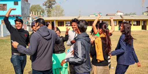 Nepalese youth gather and lift their hands in celebration outside a university
