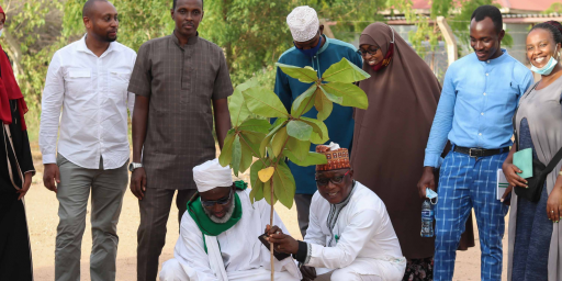 Pastor James Wuye and Imam Muhammad Ashafa plant a tree while a group looks on, smiling